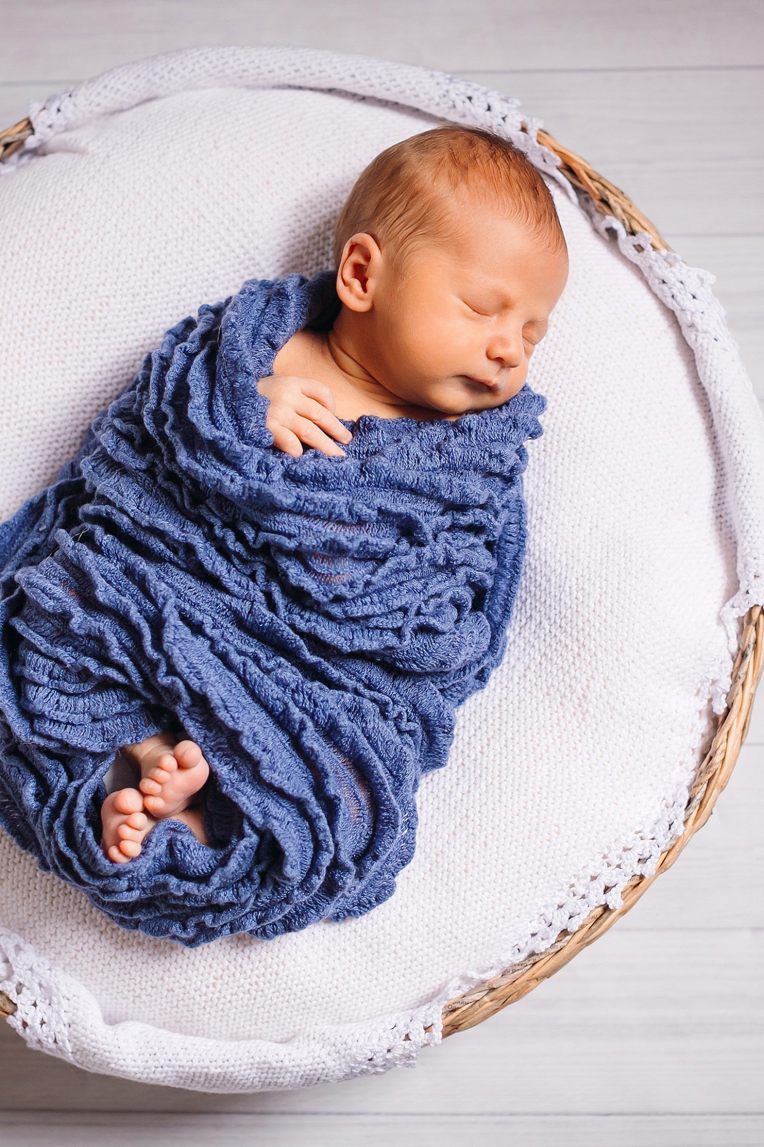 Newborn baby enveloped in blue scarf sleeps on white pillow